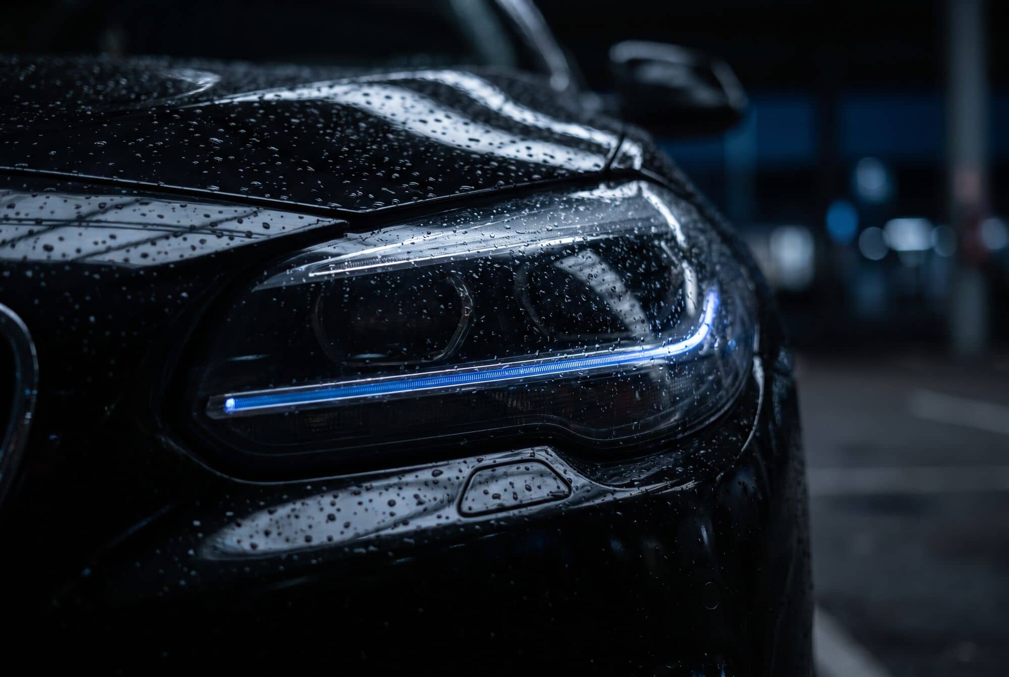Farol de um carro preto coberto de gotas de água, com um traço de luz azul